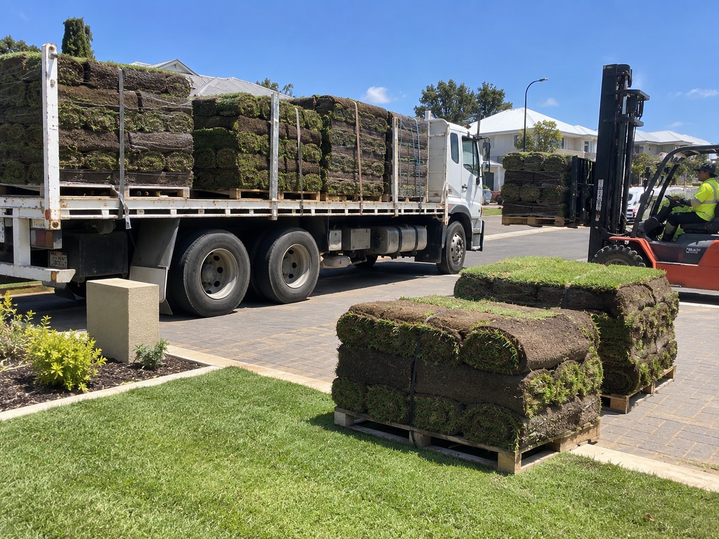 Truck and forklift unloading pallets of turf rolls for a commercial lawn laying job in Perth